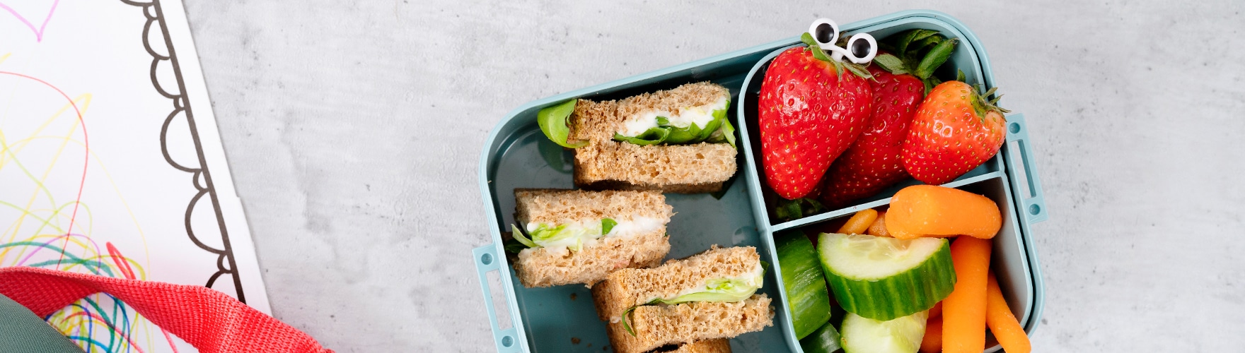 Kids’ lunch box with strawberries, cucumber, carrot and cheese spread sandwiches