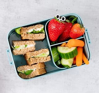 Kids’ lunch box with strawberries, cucumber, carrot and cheese spread sandwiches