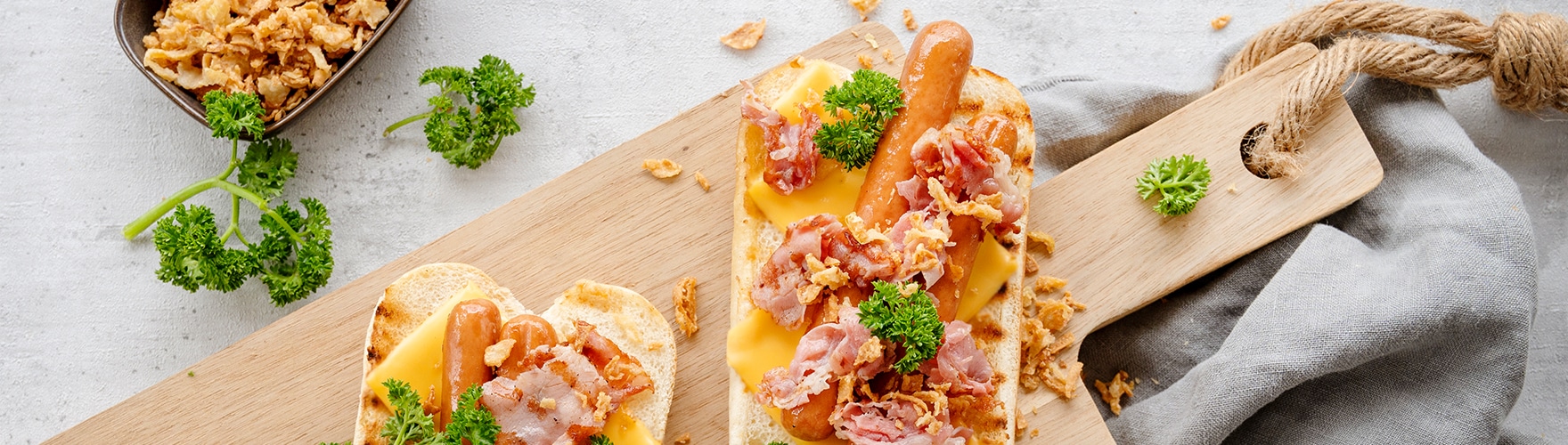 Broodje hotdog met cheddar kaas, bacon, gebakken uitjes en peterselie